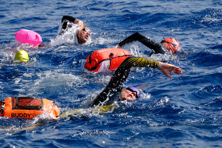 Open-Water-Schwimmerinnen und -Schwimmer mit bunten Schwimmbojen im Meer