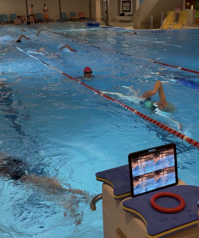 Seminar im Hallenbad: Schwimmer im Kraul, am Beckenrand ein Tablet mit der Videoanalyse